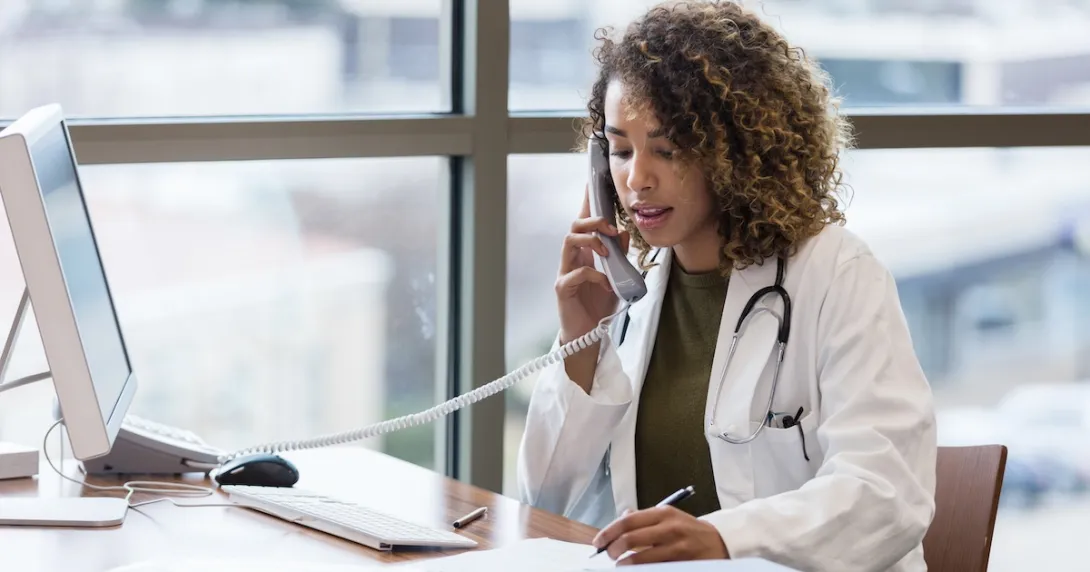 Healthcare provider on the phone while sitting at a desk with a computer on it Healthcare provider on the phone while sitting at a desk with a computer on it