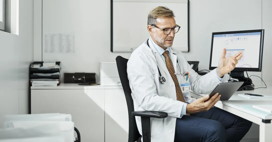 Doctor sitting in a chair at a desk while looking at a tablet Doctor sitting in a chair at a desk while looking at a tablet