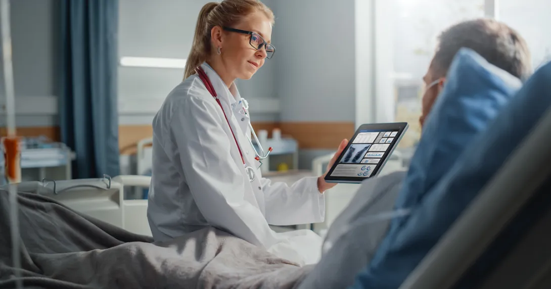 Healthcare provider sitting on a patient's hospital bed while holding a tablet showing diagnostic images of lungs
Healthcare provider sitting on a patient's hospital bed while holding a tablet showing diagnostic images of lungs