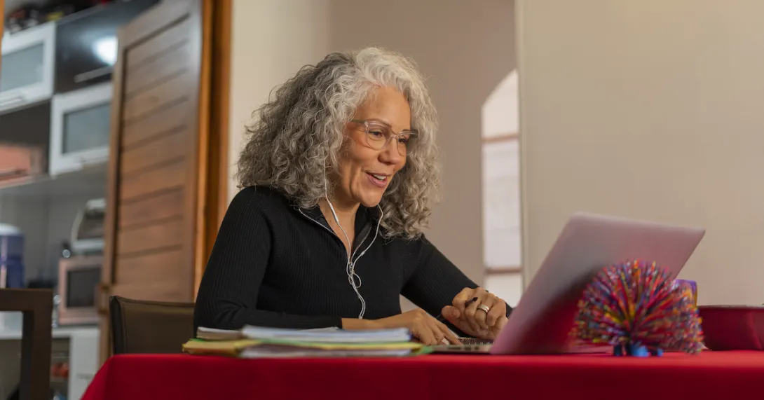 Person sitting at a table with a red table cloth on it while in a home looking at a computer
Person sitting at a table with a red table cloth on it while in a home looking at a computer