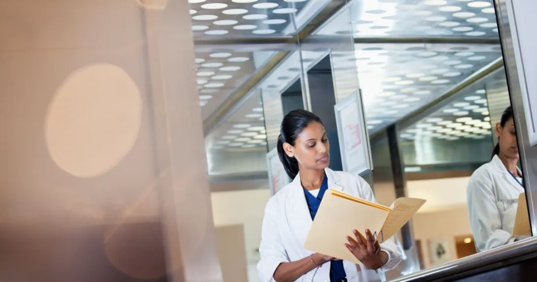 Person in lab coat looking down at file Person in lab coat looking down at file