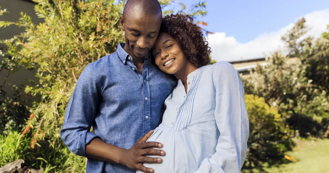 A pregnant person standing in a garden next to another person with their hand on the pregnant person's stomach
A pregnant person standing in a garden next to another person with their hand on the pregnant person's stomach