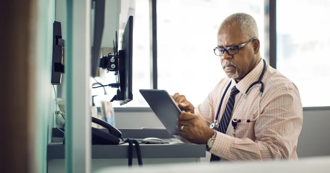 Healthcare provider sitting at a desk and looking at a tablet Healthcare provider sitting at a desk and looking at a tablet