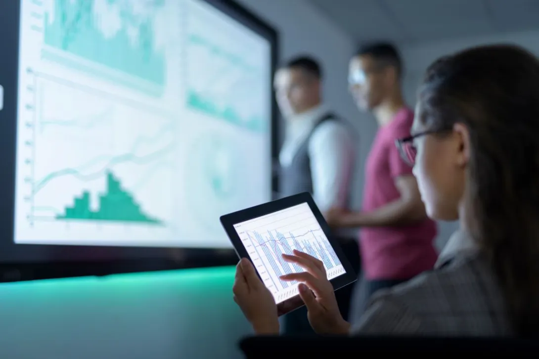 Person holds tablet while looking at information on a large screen Person holds tablet while looking at information on a large screen