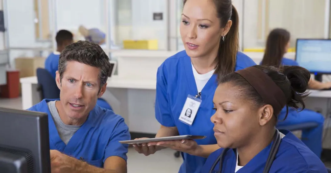 Three healthcare providers wearing scrubs sitting around a computer looking at the screen
Three healthcare providers wearing scrubs sitting around a computer looking at the screen