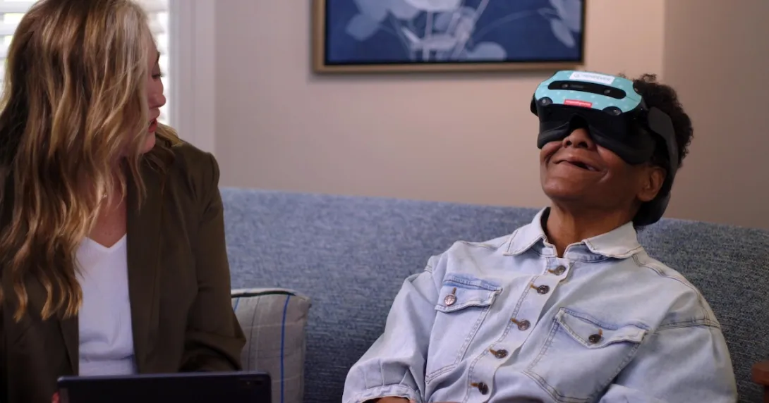 Patient using a Rendever headset while sitting next to another individual Patient using a Rendever headset while sitting next to another individual