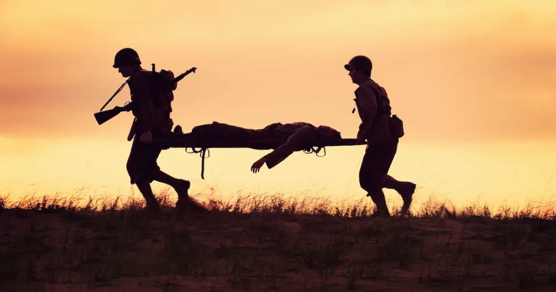 Two soldiers carrying another soldier on a gurney across a field Two soldiers carrying another soldier on a gurney across a field