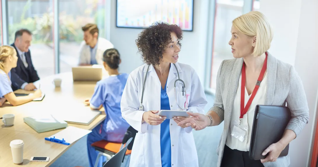 A businessperson talks with a doctor in a hospital board room.
A businessperson talks with a doctor in a hospital board room.