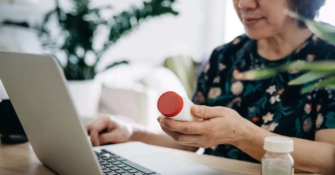 A woman holding a pill bottle and using a laptop.
A woman holding a pill bottle and using a laptop.