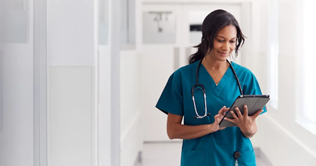 Healthcare provider wearing scrubs with a stethoscope around their neck while walking down the hallway of a health center Healthcare provider wearing scrubs with a stethoscope around their neck while walking down the hallway of a health center