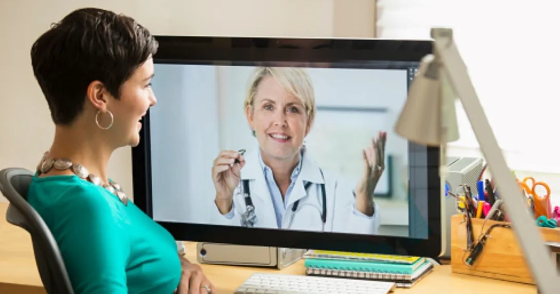 Person with green shirt talks with person on computer monitor in lab coat Person with green shirt talks with person on computer monitor in lab coat