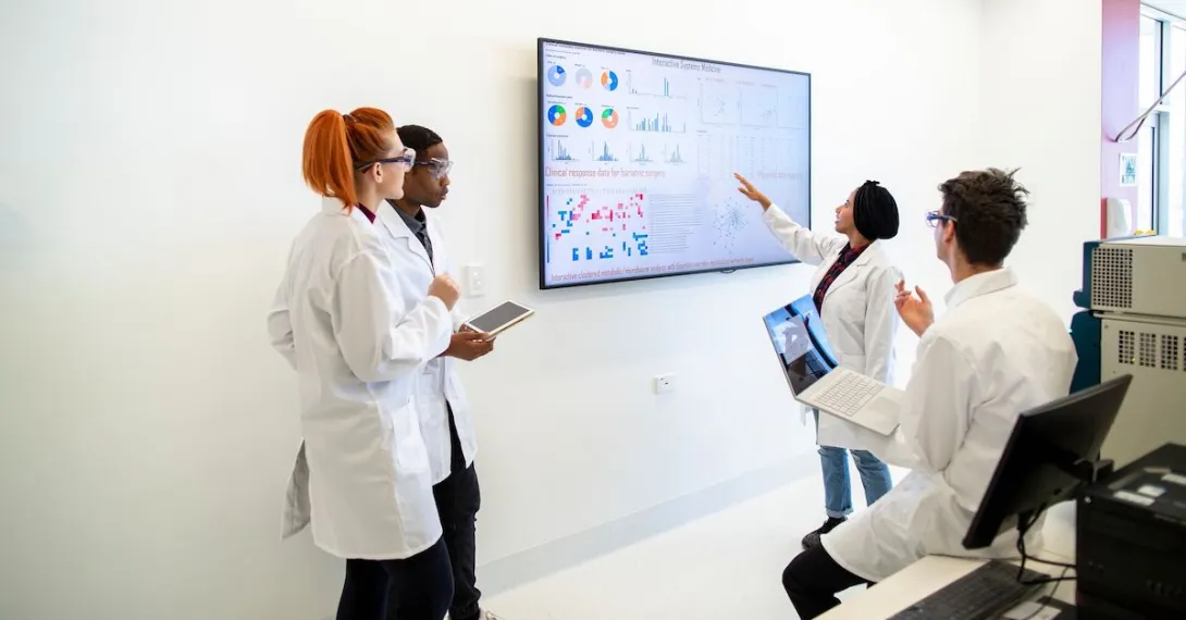 A group of researchers gathered around a screen displaying charts and data.
A group of researchers gathered around a screen displaying charts and data.