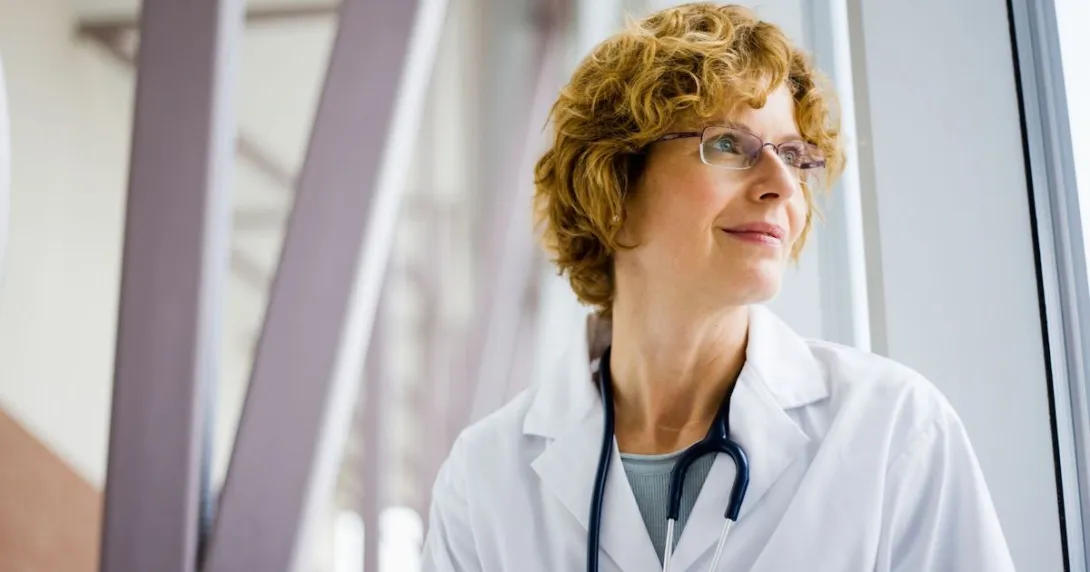 Healthcare provider wearing a stethoscope and looking out a window Healthcare provider wearing a stethoscope and looking out a window