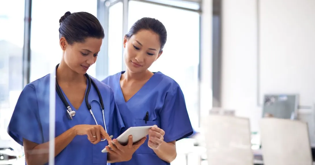 Two healthcare professionals standing next to each other while looking at a tablet Two healthcare professionals standing next to each other while looking at a tablet
