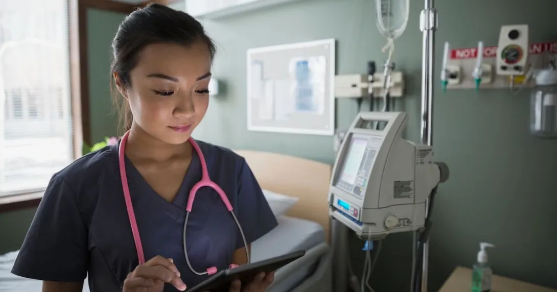 Healthcare provider standing in a hospital room wearing a pink stethoscope while holding a tablet
Healthcare provider standing in a hospital room wearing a pink stethoscope while holding a tablet