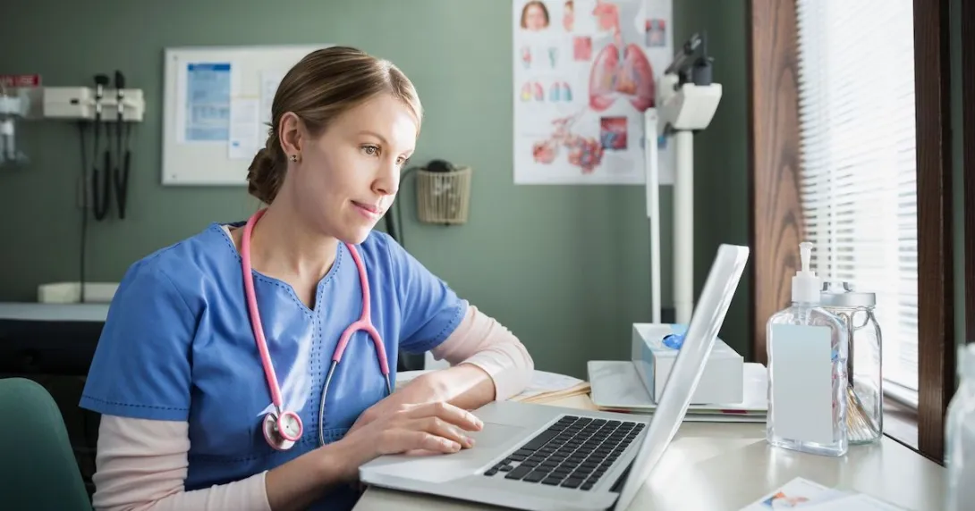 Healthcare provider in scrubs sitting at a desk and looking at a computer
Healthcare provider in scrubs sitting at a desk and looking at a computer