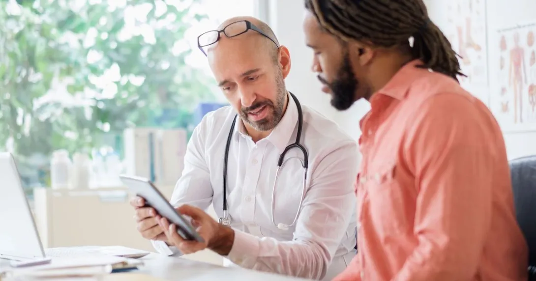 Healthcare provider sitting next to another individual while both are looking at a tablet Healthcare provider sitting next to another individual while both are looking at a tablet