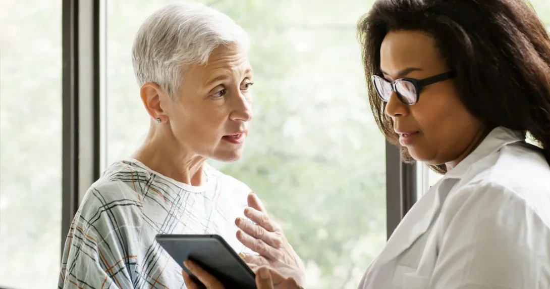 Healthcare provider talking to a patient in a hospital gown while both look at a tablet
Healthcare provider talking to a patient in a hospital gown while both look at a tablet