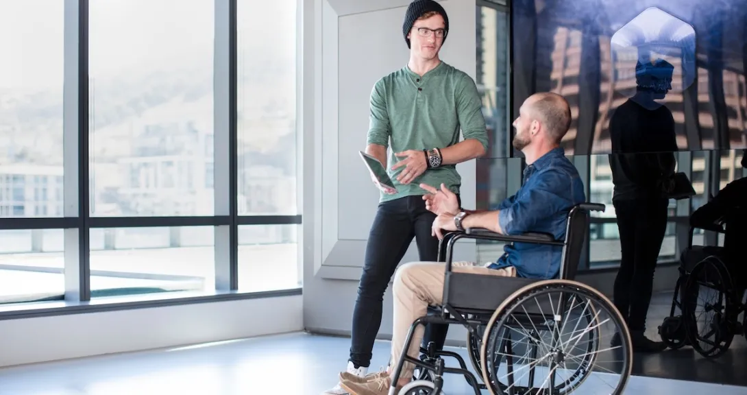 Person in a wheelchair and another people standing beside them in a room with a large window Person in a wheelchair and another people standing beside them in a room with a large window