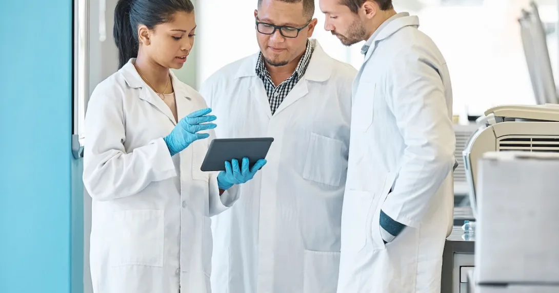 Three healthcare professionals standing in a circle looking at a tablet Three healthcare professionals standing in a circle looking at a tablet