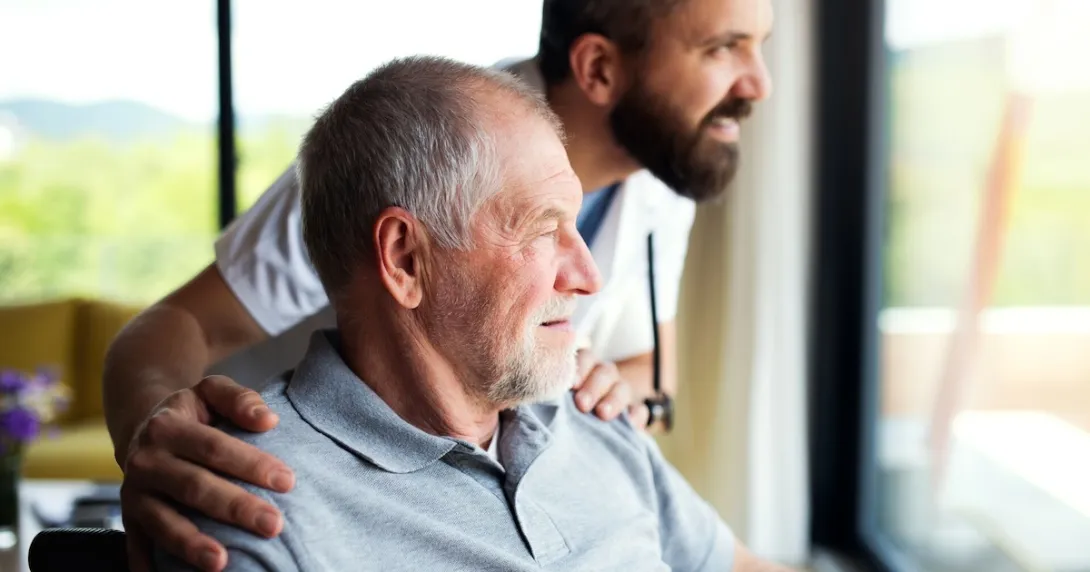 Person sitting in a chair while looking out a window with another person standing beside them Person sitting in a chair while looking out a window with another person standing beside them