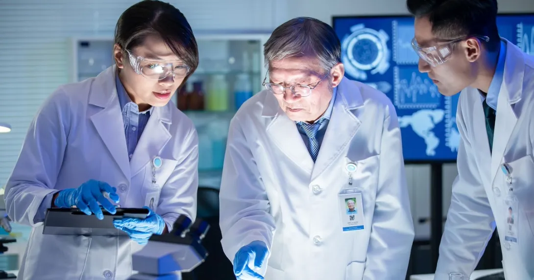 Three healthcare professionals in lab coats looking at something under a light Three healthcare professionals in lab coats looking at something under a light