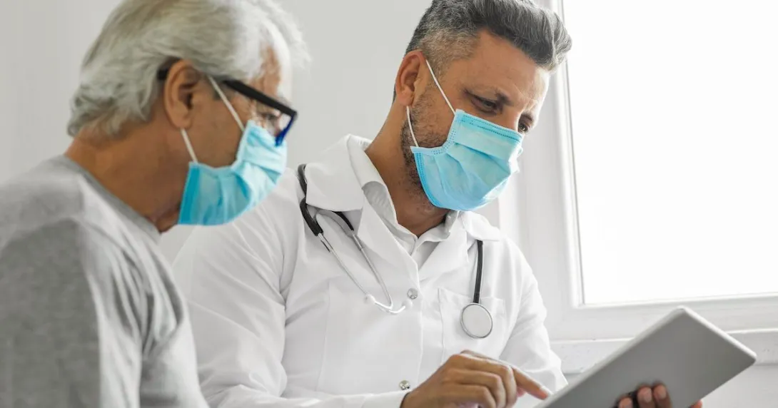 Healthcare provider sitting with a patient while looking at a tablet Healthcare provider sitting with a patient while looking at a tablet