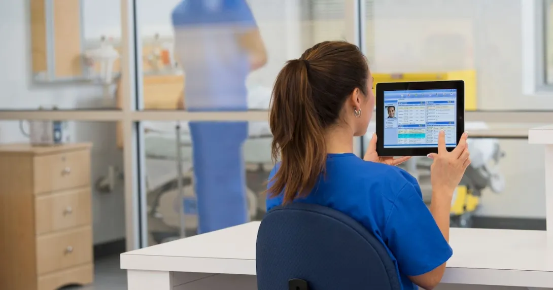 Healthcare provider in the clinical setting sitting at a desk and looking at a tablet Healthcare provider in the clinical setting sitting at a desk and looking at a tablet