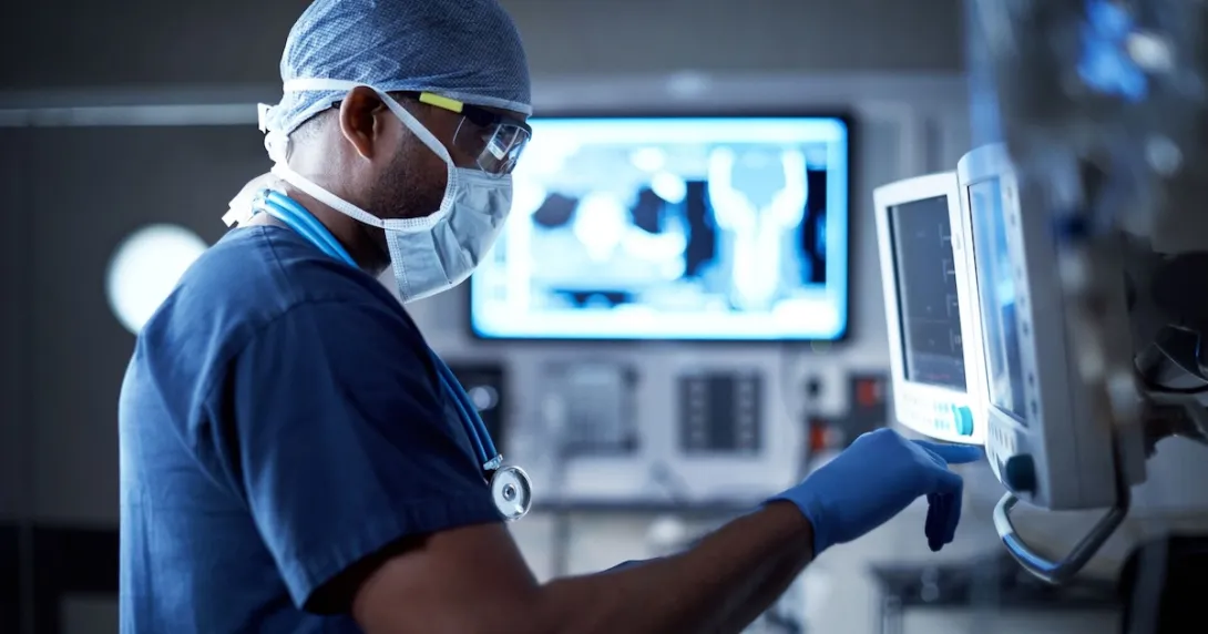 Doctor in scrubs standing in front of computer screens Doctor in scrubs standing in front of computer screens