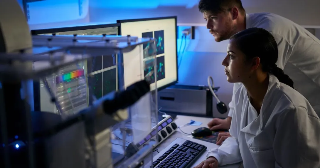 Two healthcare professionals, one sitting down and one standing up, looking at computer screens in a dark room
Two healthcare professionals, one sitting down and one standing up, looking at computer screens in a dark room