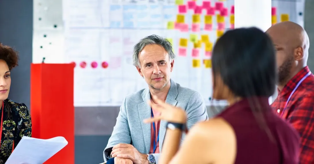 People sitting around a table in front of a whiteboard talking to each other
People sitting around a table in front of a whiteboard talking to each other