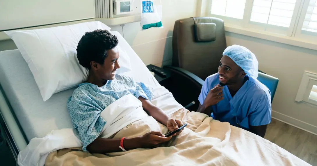Healthcare provider sitting next to a hospital bed with a teenager in it looking at a phone
Healthcare provider sitting next to a hospital bed with a teenager in it looking at a phone