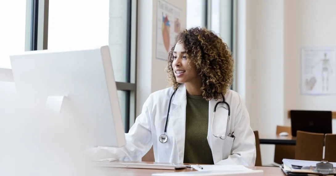 A doctor reviewing a patient record on a desktop computer A doctor reviewing a patient record on a desktop computer