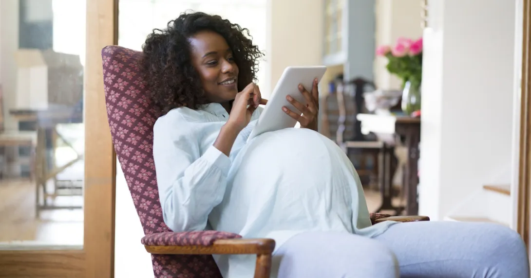 Pregnant person sitting in a chair, looking at a tablet Pregnant person sitting in a chair, looking at a tablet