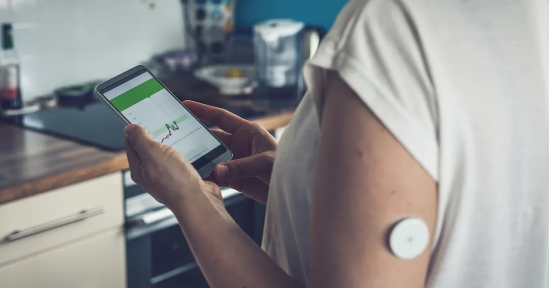 Person with a continuous glucose monitor checks their health data on a smartphone app