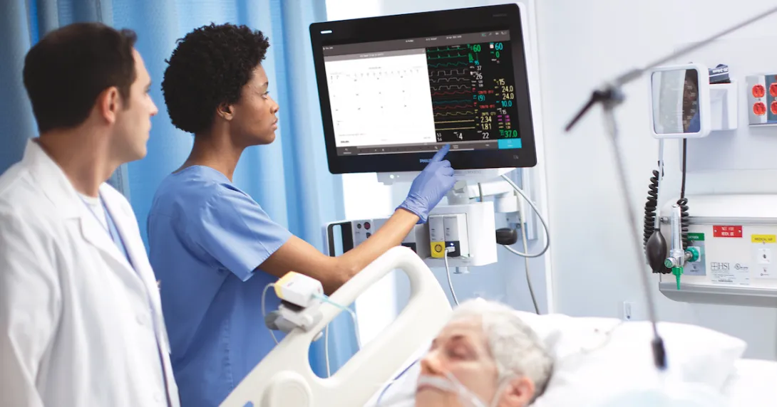 Providers using the new patient monitor next to a bed where a patient is sleeping Providers using the new patient monitor next to a bed where a patient is sleeping