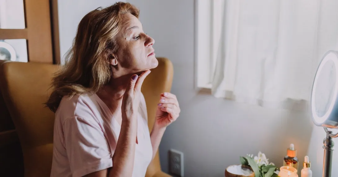Person applying skincare treatment to their neck in front of a mirror