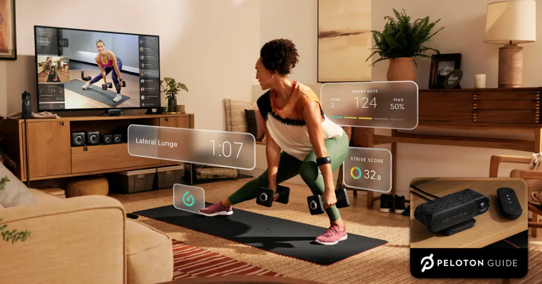 A woman lifting weights using the Peloton Guide while watching an instructor on her TV A woman lifting weights using the Peloton Guide while watching an instructor on her TV