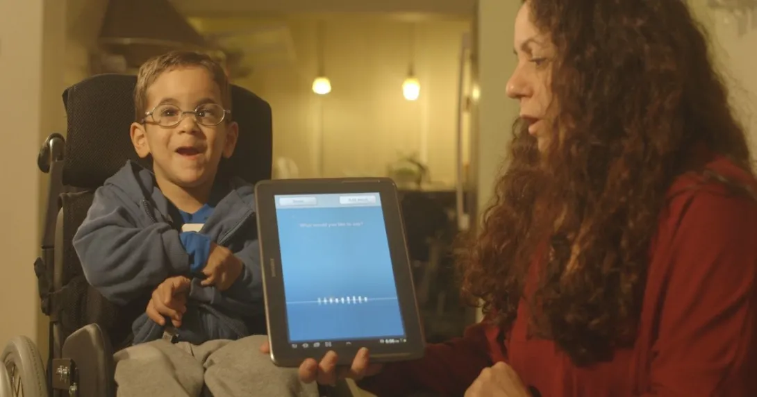 Boy in a wheelchair uses Voiceitt with the help of a caregiver