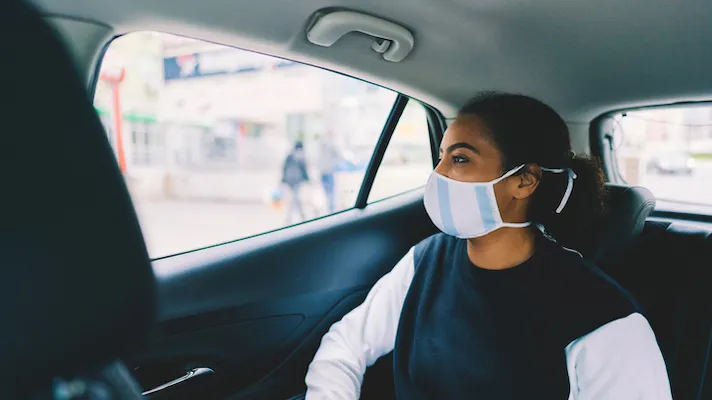 Person in a face mask sits in the back of a car looking out the window