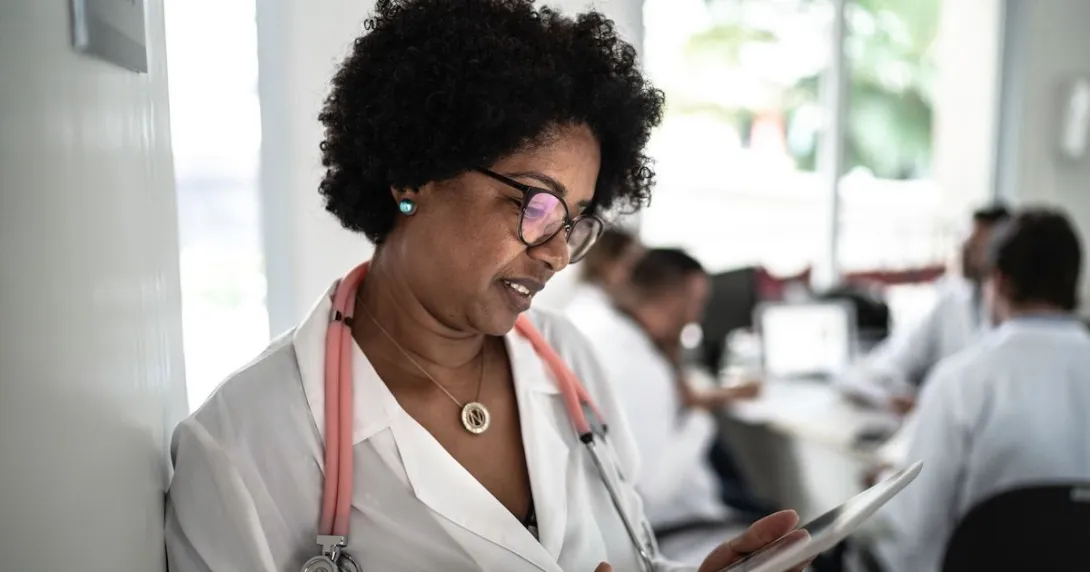 A doctor looking a tablet while a meeting occurs in the background A doctor looking a tablet while a meeting occurs in the background
