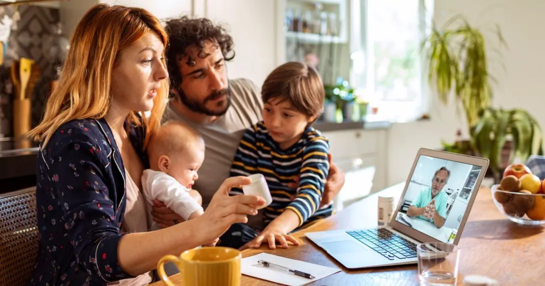 Parents with two young children talk to a provider through a video call on their laptop. Parents with two young children talk to a provider through a video call on their laptop.