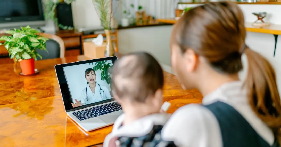 A mom holding a baby talking to a doctor via telehealth A mom holding a baby talking to a doctor via telehealth