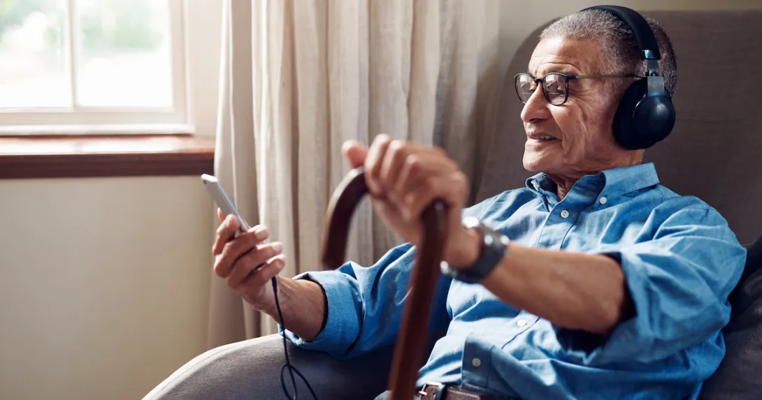 An older man wearing headphones and holding a smartphone An older man wearing headphones and holding a smartphone