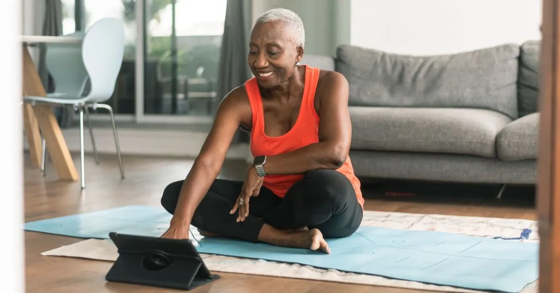 A person using a tablet while sitting on a yoga mat and preparing to exercise A person using a tablet while sitting on a yoga mat and preparing to exercise