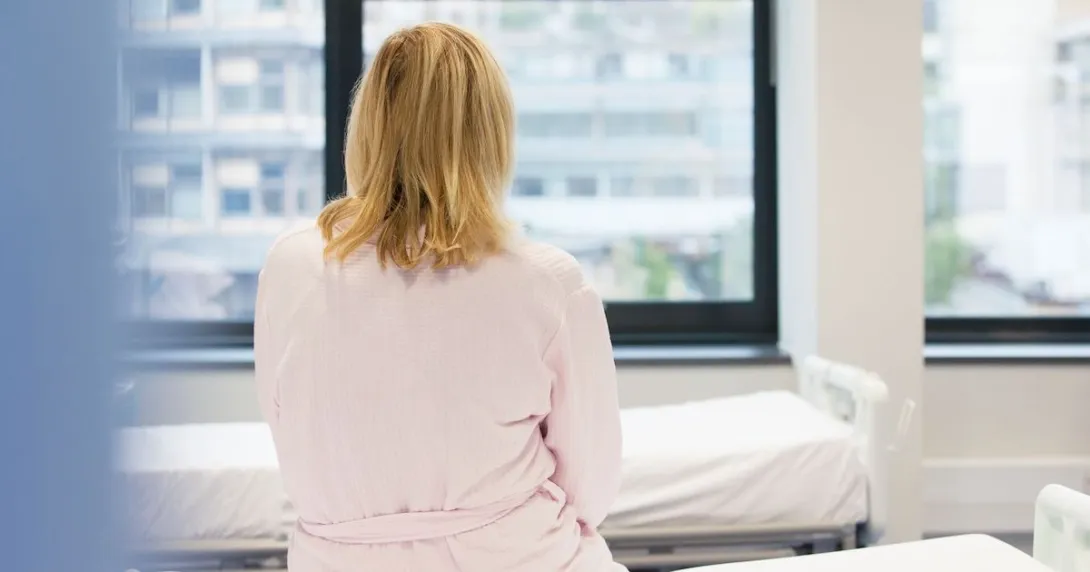A person sitting on a hospital bed with her back to the camera. A person sitting on a hospital bed with her back to the camera.
