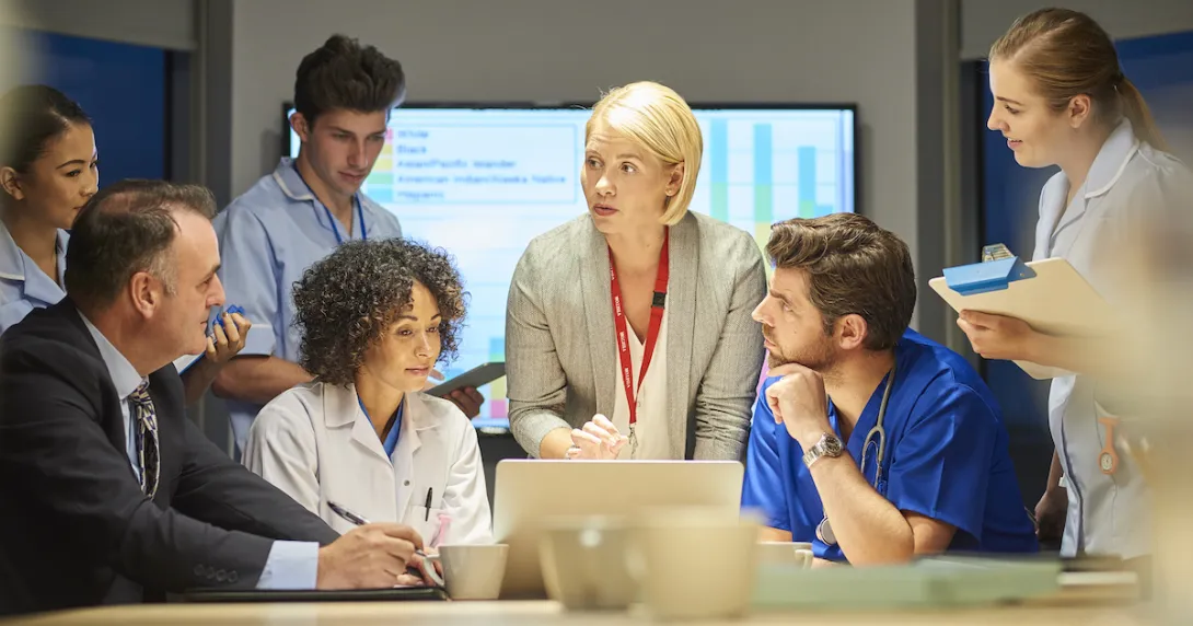 Several people standing and sitting around a table with a screen in the background that has a graph on it