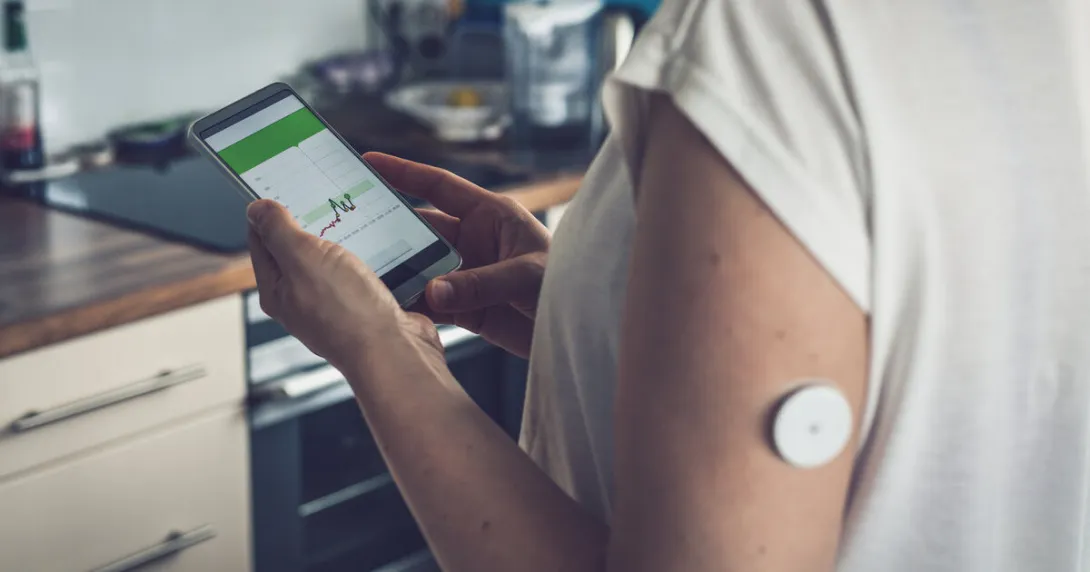 A person wearing a CGM patch is checking their blood glucose level on a mobile app