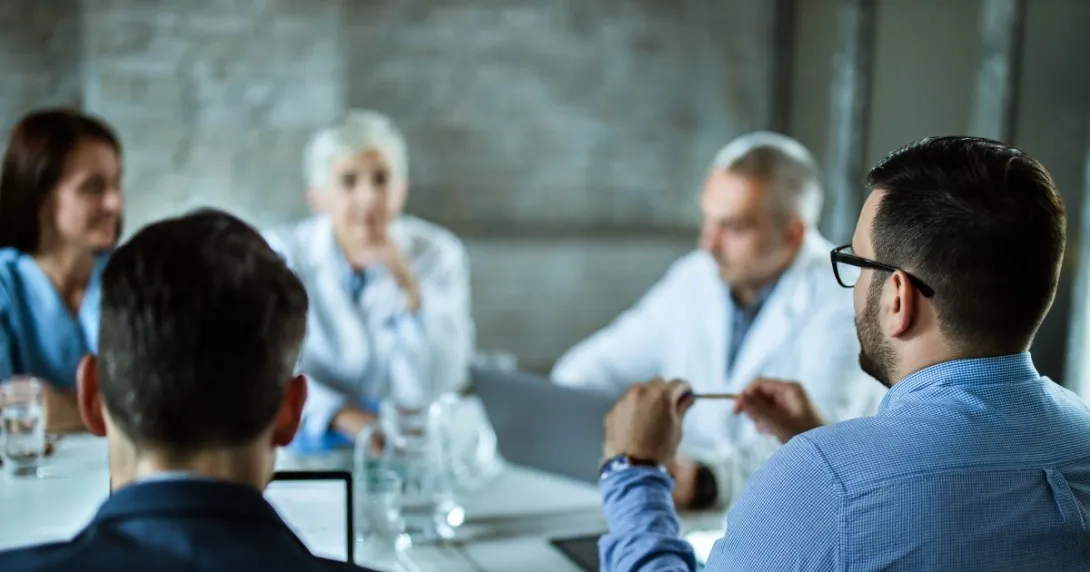 Group of people, two in lab coats, sit around table
