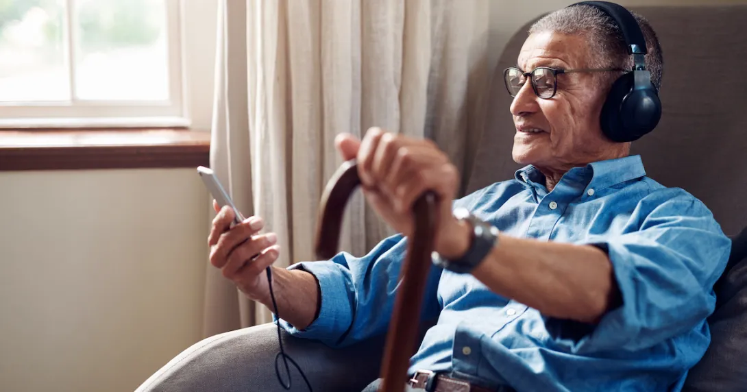 Person sitting in a chair while holding a cane and phone while wearing headphones